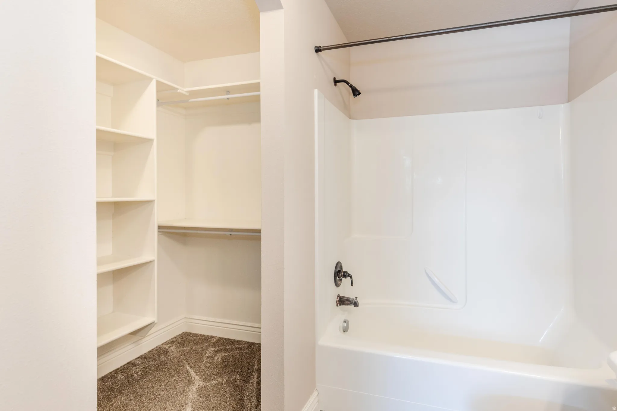 Combination tub/shower with dark bronze fixtures and a walk-in closet featuring built-in shelving and hanging rods over patterned carpet