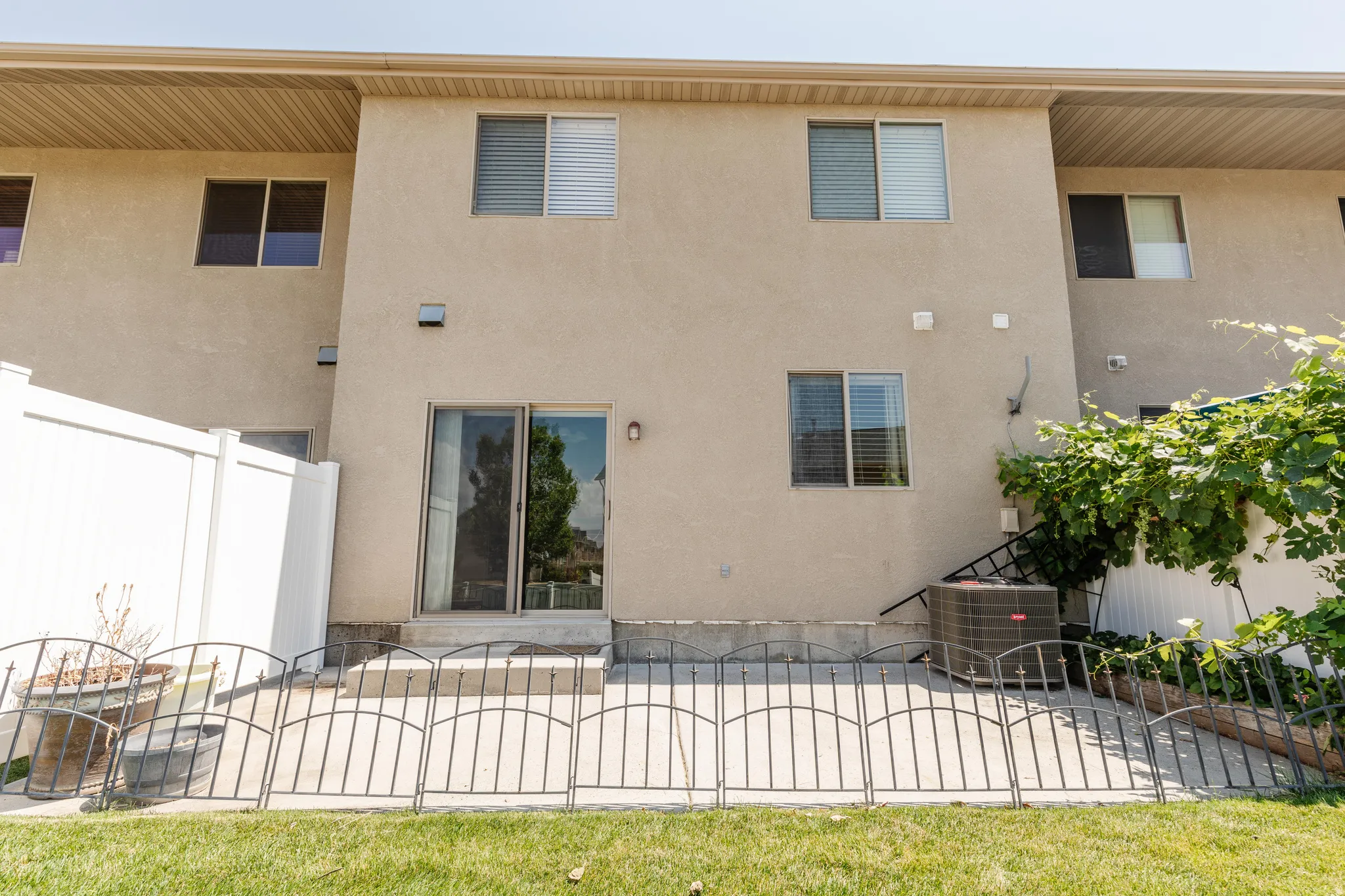 Rear exterior featuring a sliding glass door, a concrete patio, a vinyl fence, multiple windows, and stucco siding
