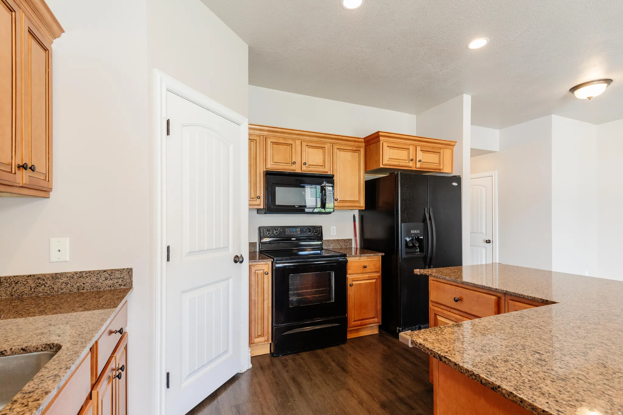 Kitchen featuring wood cabinetry, black appliances, granite countertops, and wood-finish flooring
