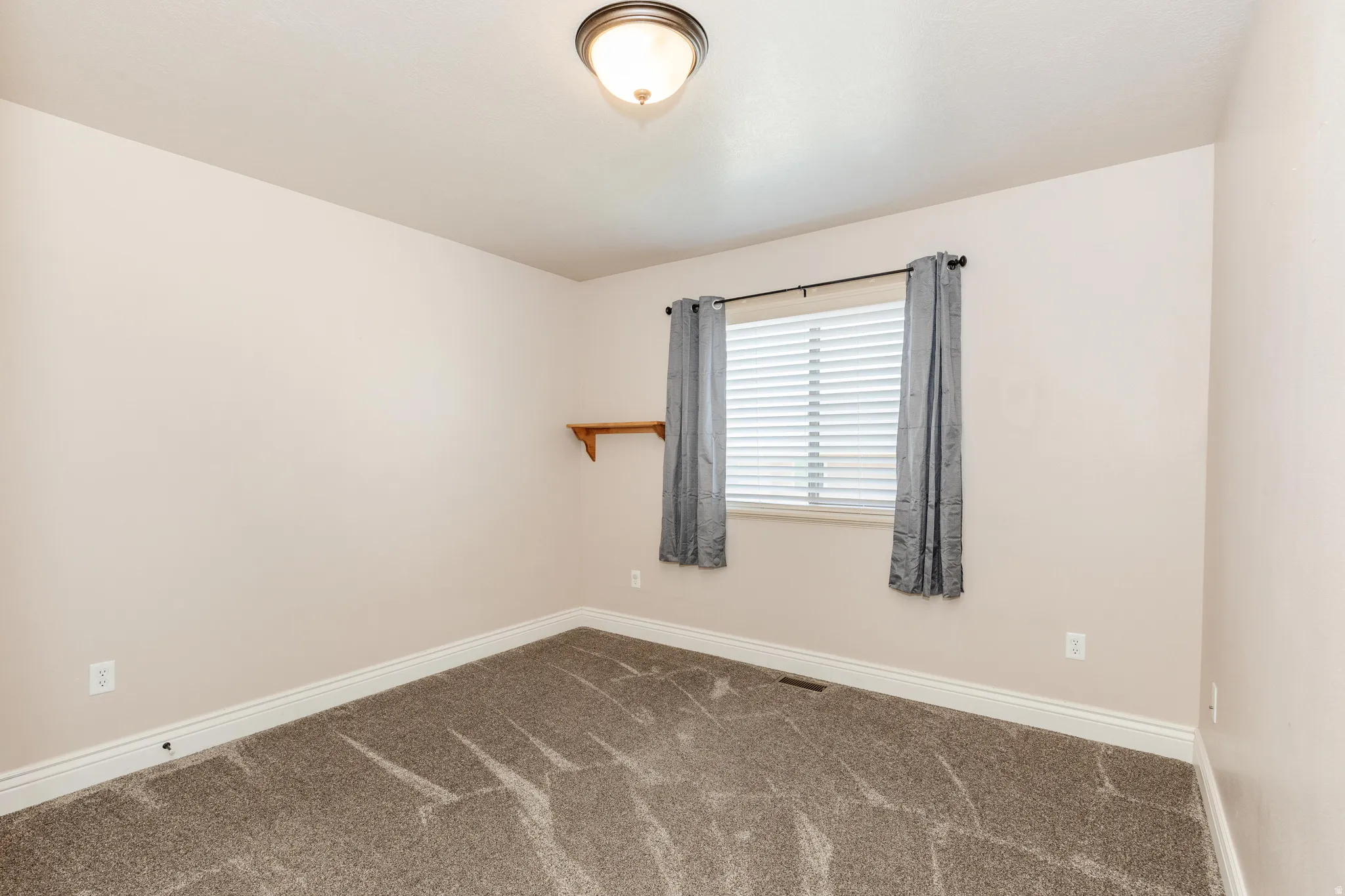 Neutral-toned interior room with patterned carpeting, a single window with blinds, and a ceiling-mounted light fixture