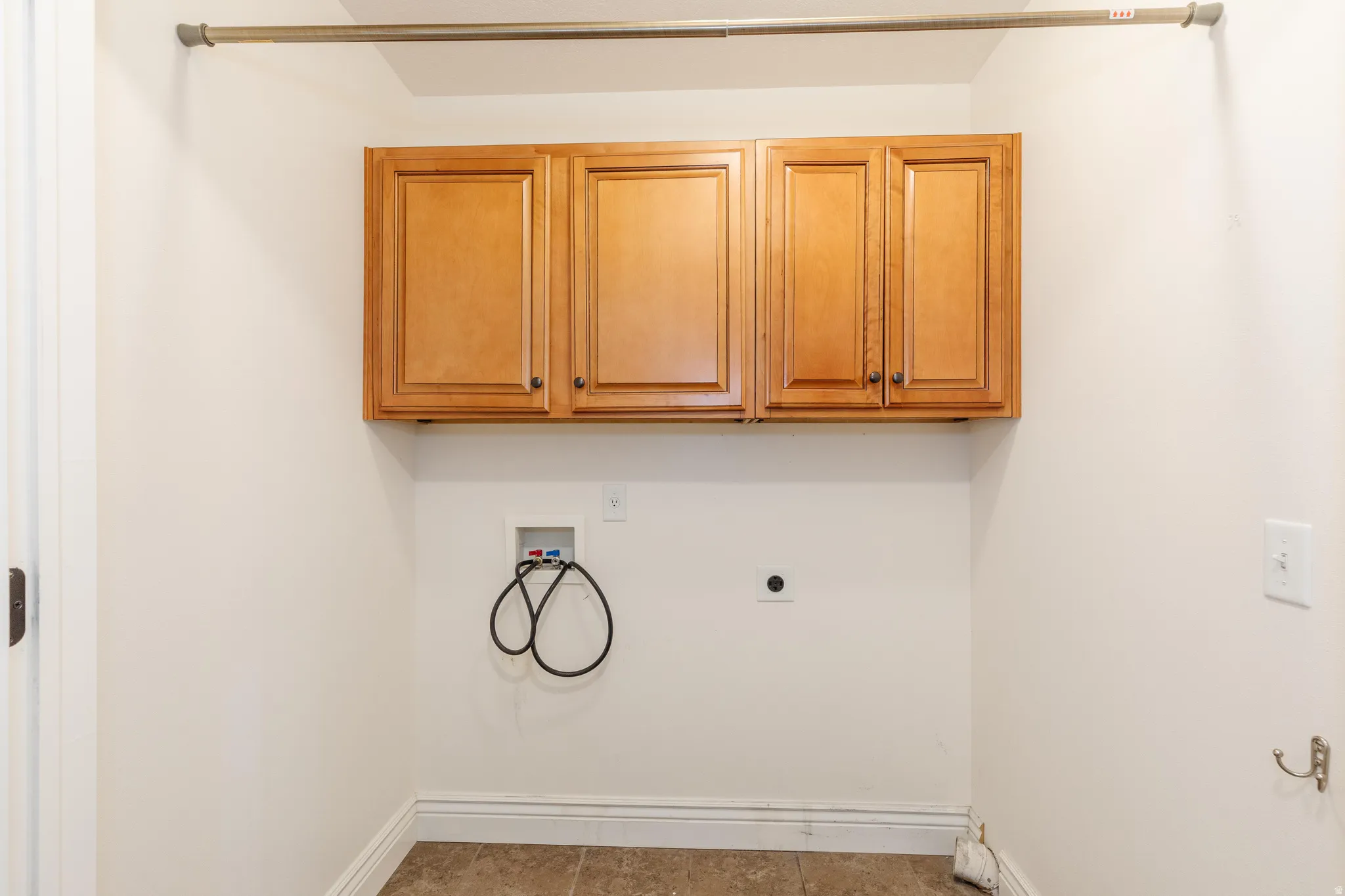 Laundry area featuring light wood-finish cabinetry, tile flooring, and a chrome hanging rod