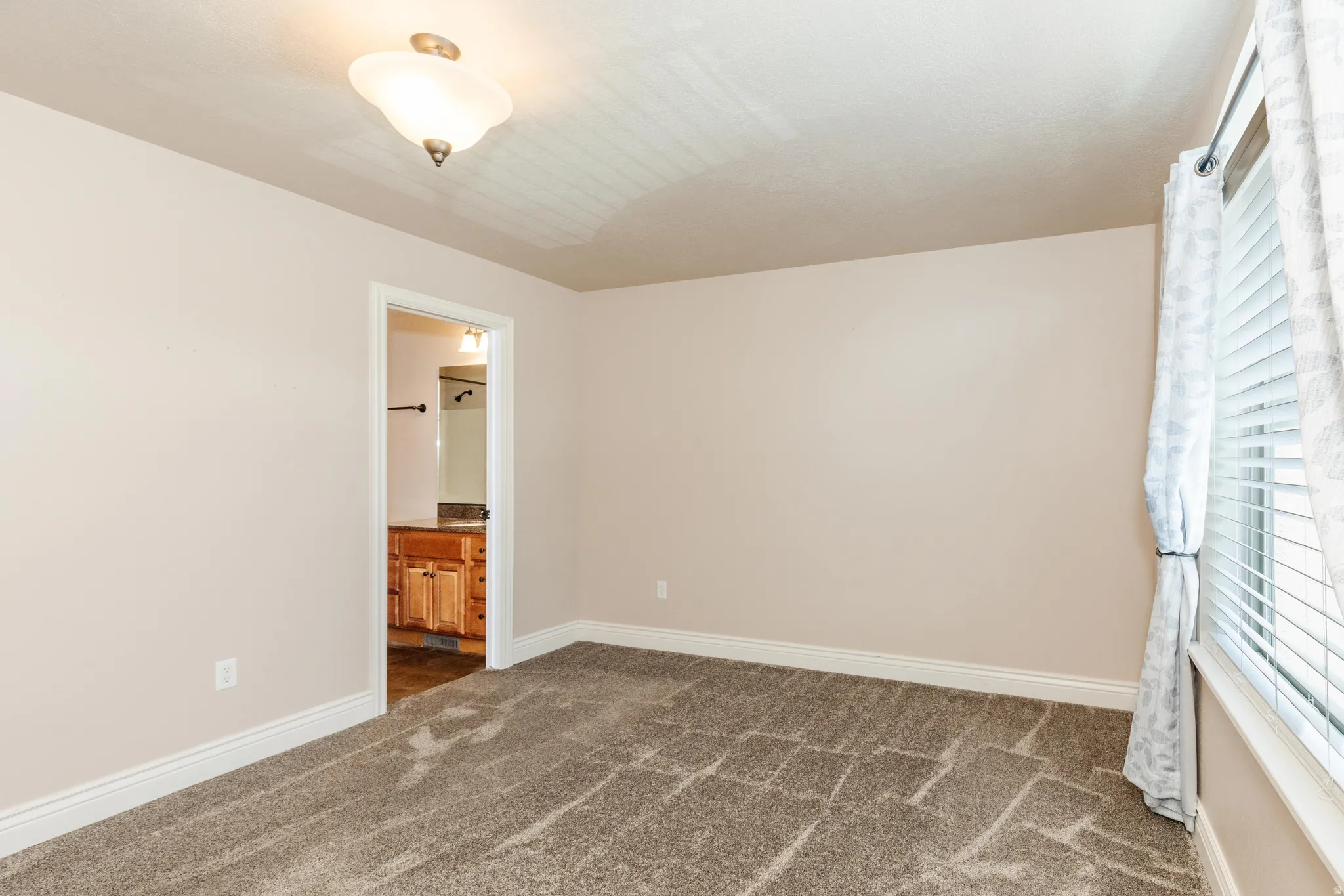 Carpeted room with a ceiling-mounted light fixture and a window featuring blinds and curtains
