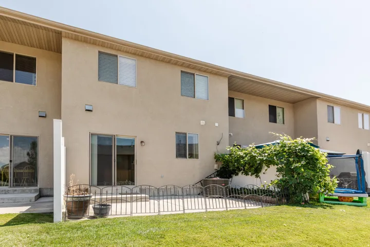 Expansive grassy backyard featuring two sliding glass doors, multiple windows, and an outdoor patio space