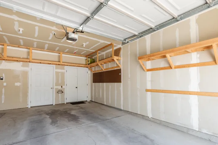 Attached garage featuring a concrete floor, built-in wooden shelving, and a garage door opener