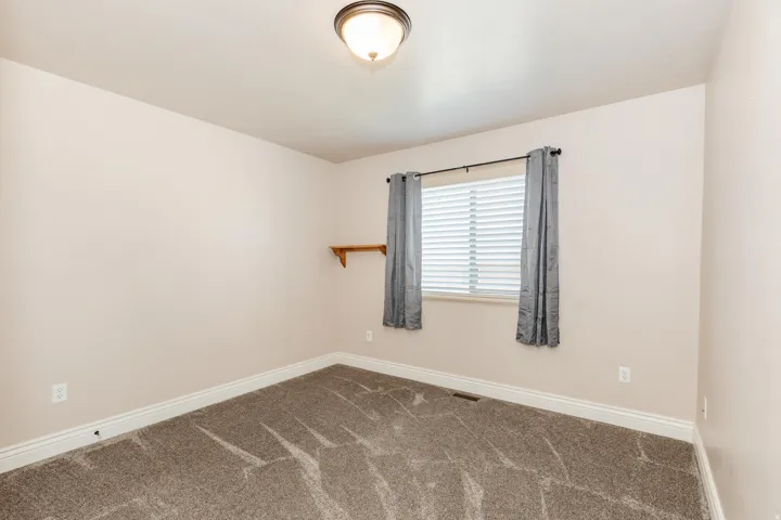 Neutral-toned interior room with patterned carpeting, a single window with blinds, and a ceiling-mounted light fixture