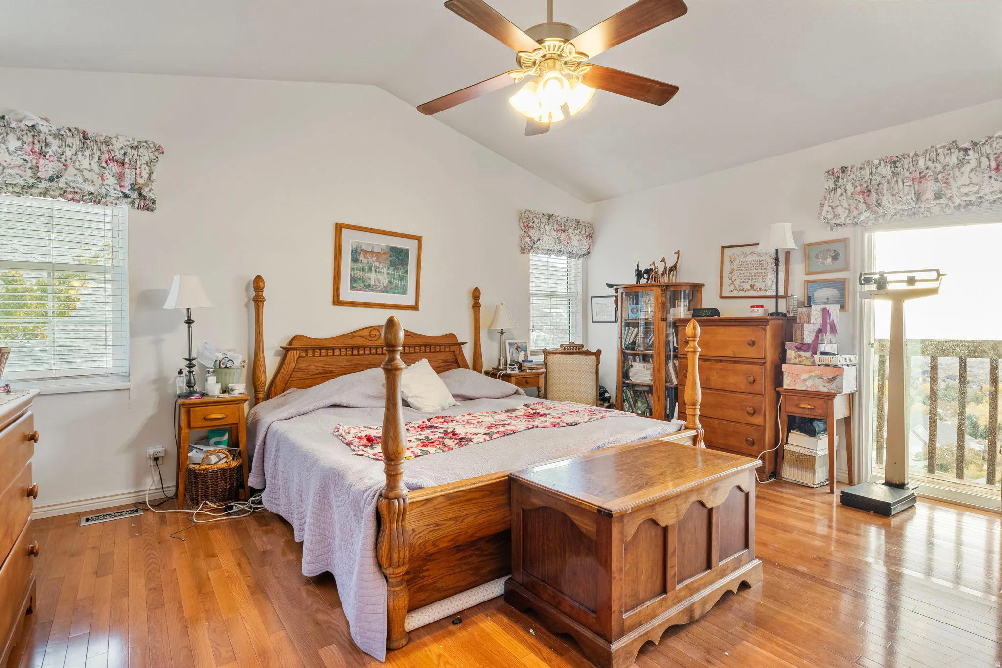 Vaulted ceiling bedroom featuring wood-finish flooring, a ceiling fan with integrated lighting, and multiple windows with blinds