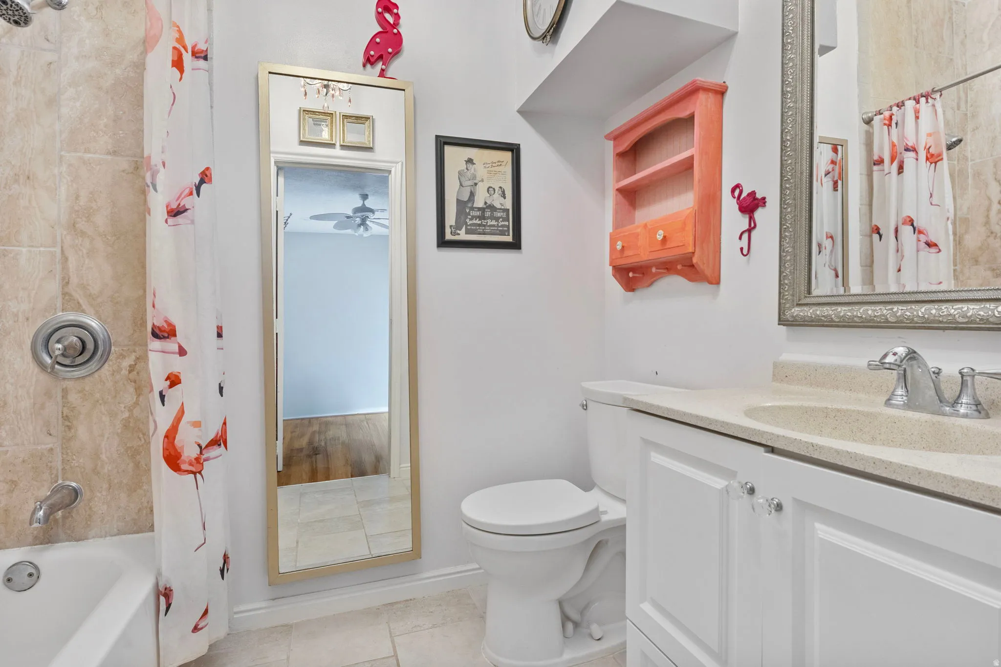 Bathroom featuring a shower/tub combination with tiled surround, a white vanity with integrated sink, a toilet, and light-toned floor tiles