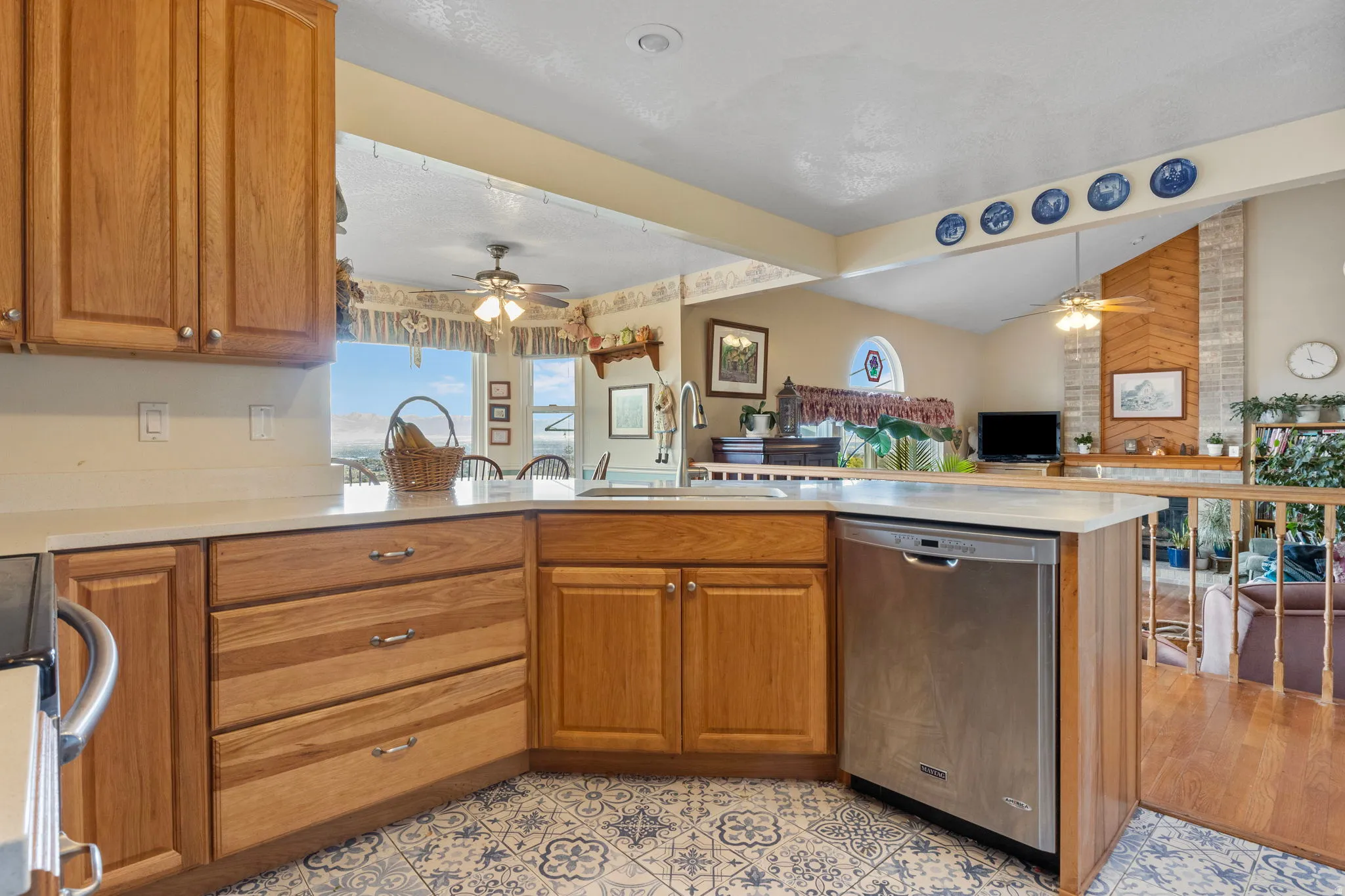 Kitchen featuring wood cabinetry, light-toned countertops, an integrated stainless steel dishwasher, and patterned floor tiling