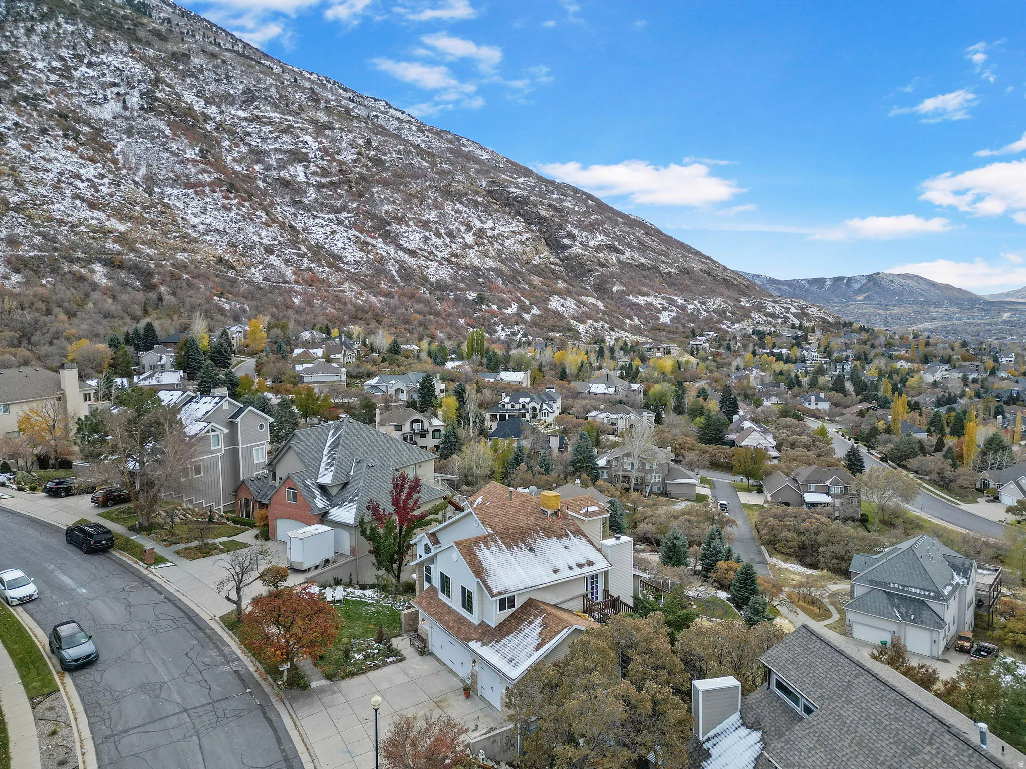 Residential neighborhood with mature trees and a curving street, set against a snow-dusted mountain backdrop