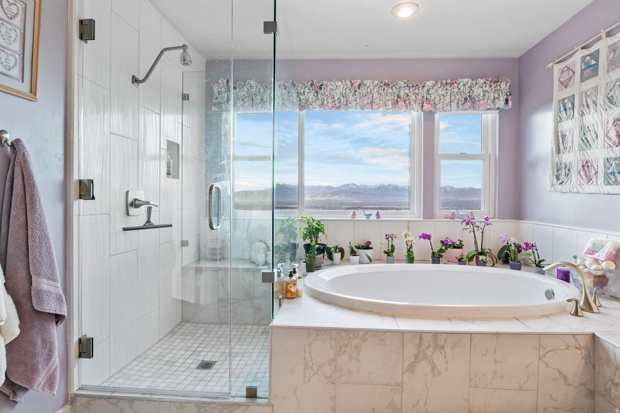 Oval soaking tub with tiled surround, framed by multiple windows and a mountain backdrop