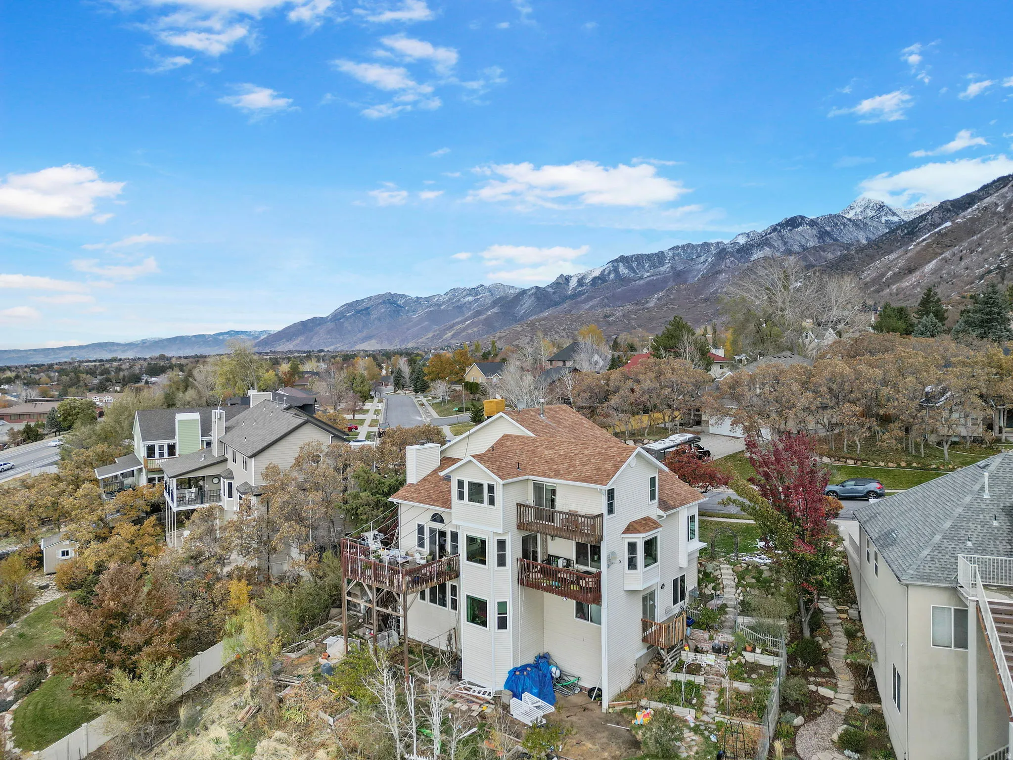 Multi-level residence featuring a light-colored exterior, brown shingle roofing, multiple balconies, and a terraced rear yard
