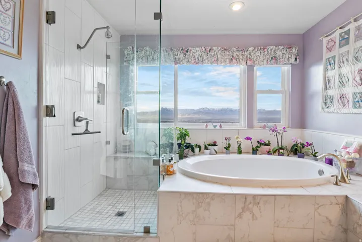 Oval soaking tub with tiled surround, framed by multiple windows and a mountain backdrop