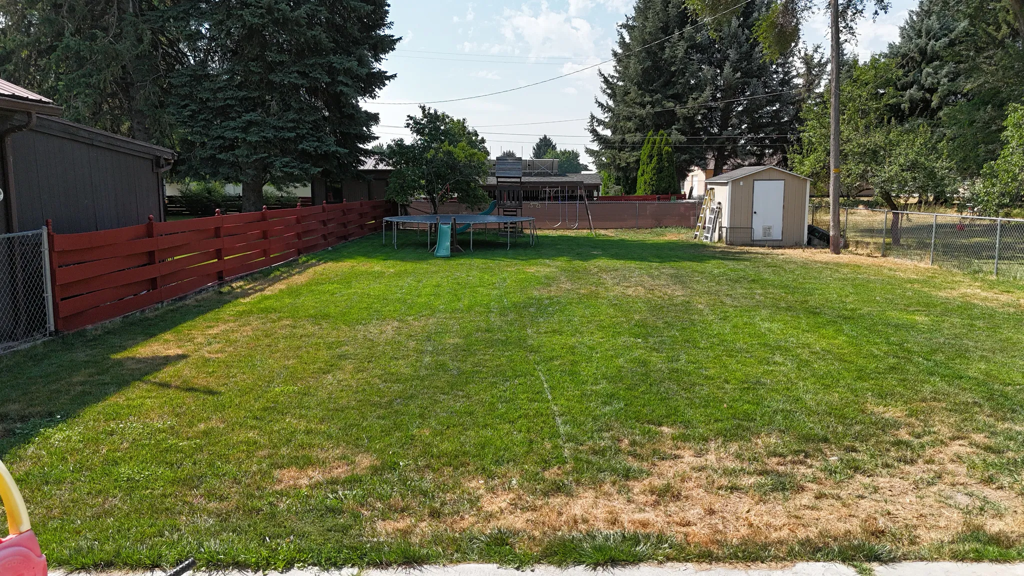Expansive grassy yard area with a painted wood fence, chain-link fencing, and mature trees