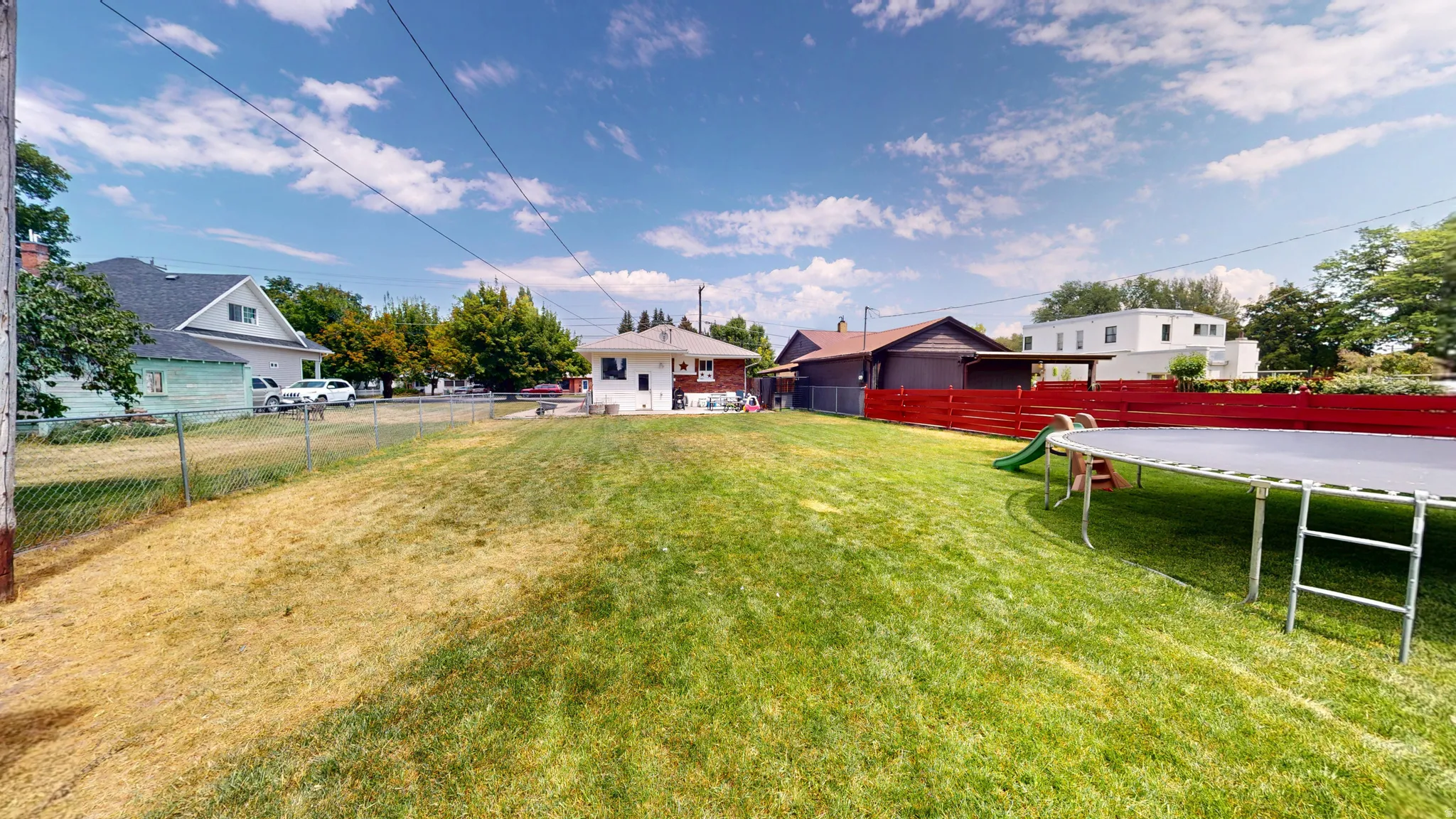 Spacious backyard featuring a large grassy area, a red privacy fence, and partial chain link fencing