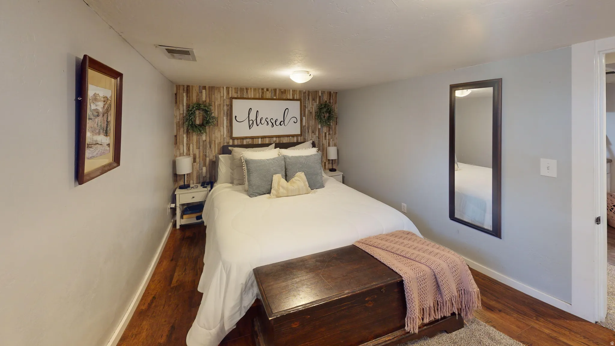 Bedroom featuring wood-finish flooring, accent wall with vertical wood paneling, light gray painted walls, and an overhead flush-mount light fixture