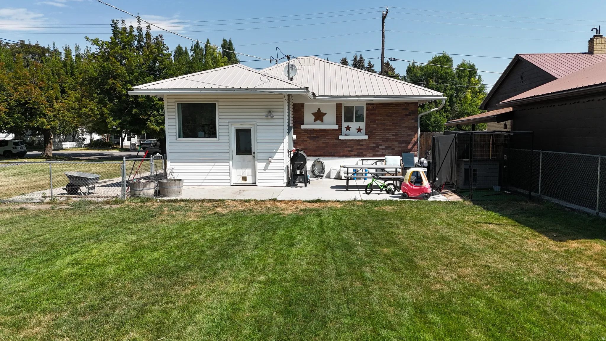Expansive backyard featuring a large concrete patio, chain-link fencing, mature trees, and a combination of brick and siding exterior finishes