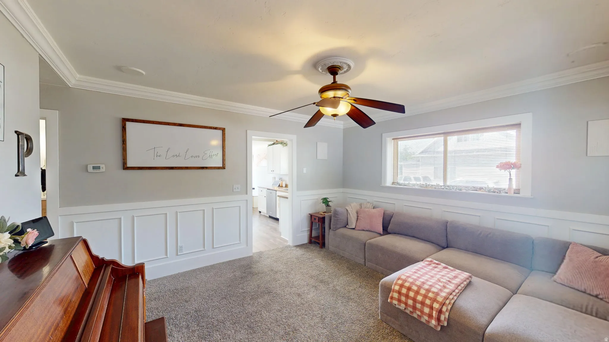 Living area featuring crown molding, wainscoting, a ceiling fan with light fixture, and a large window