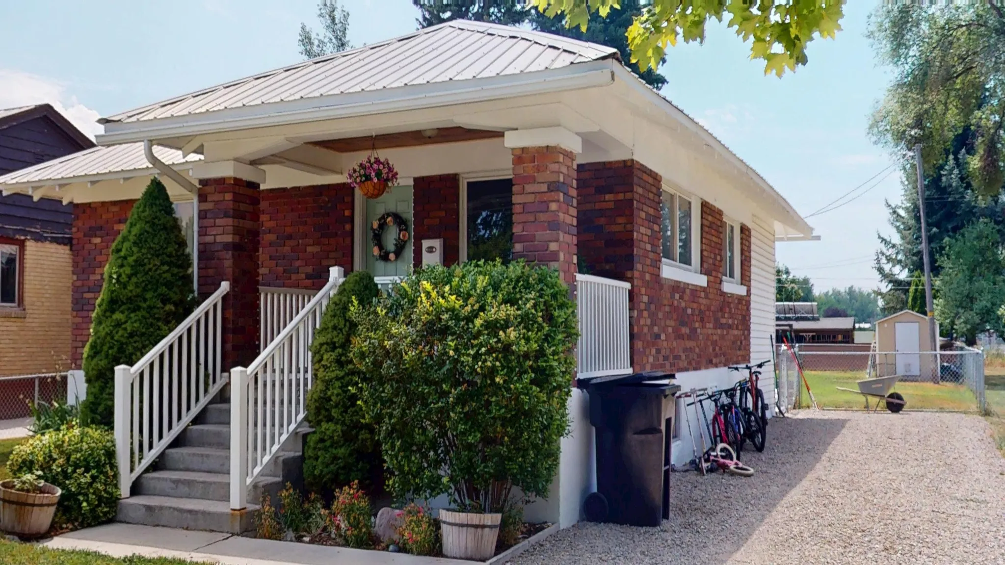 Brick facade home featuring a covered front porch with white railings, a metal roof, and a gravel driveway