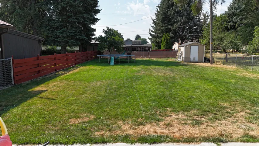Expansive grassy yard area with a painted wood fence, chain-link fencing, and mature trees