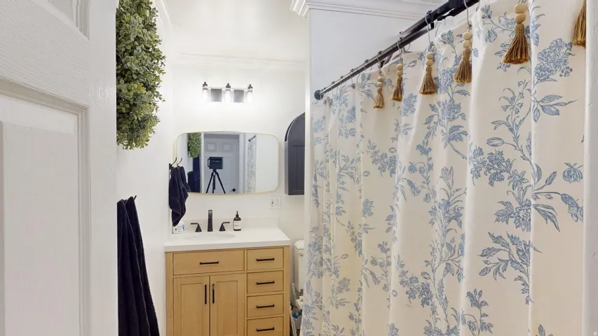 Bathroom vanity featuring a light wood cabinet with black hardware, a white countertop, and a rectangular gold-framed mirror