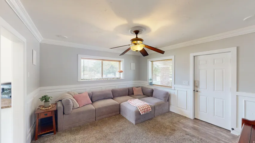 Living area featuring a ceiling fan with light fixture, crown molding, and wainscoting details