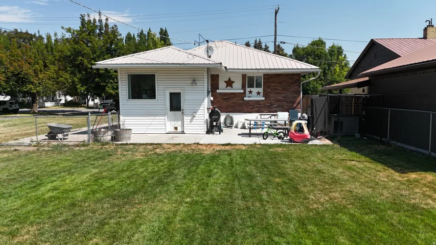 Expansive backyard featuring a large concrete patio, chain-link fencing, mature trees, and a combination of brick and siding exterior finishes