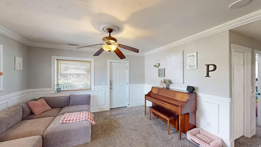 Living area featuring wainscoting, crown molding, a ceiling fan with integrated lighting, and carpet flooring