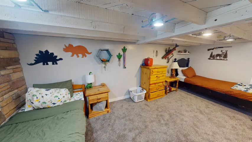 Spacious room featuring exposed white-painted ceiling beams, light gray wall paint, and gray carpeted flooring