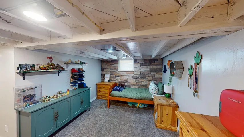 Finished room featuring exposed white-washed ceiling beams, carpet flooring, a stone-accented wall, and recessed lighting