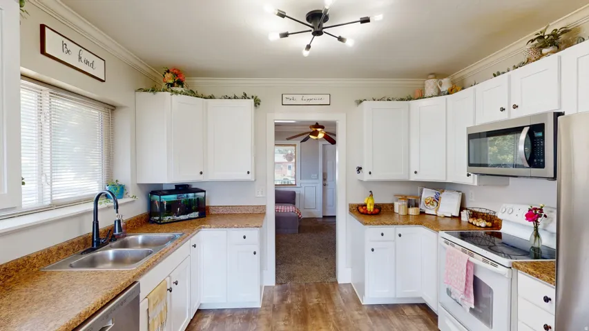 Well-appointed kitchen featuring white cabinetry, wood-finish flooring, a stainless steel double-basin sink with a matte black faucet, and a built-in stainless steel microwave