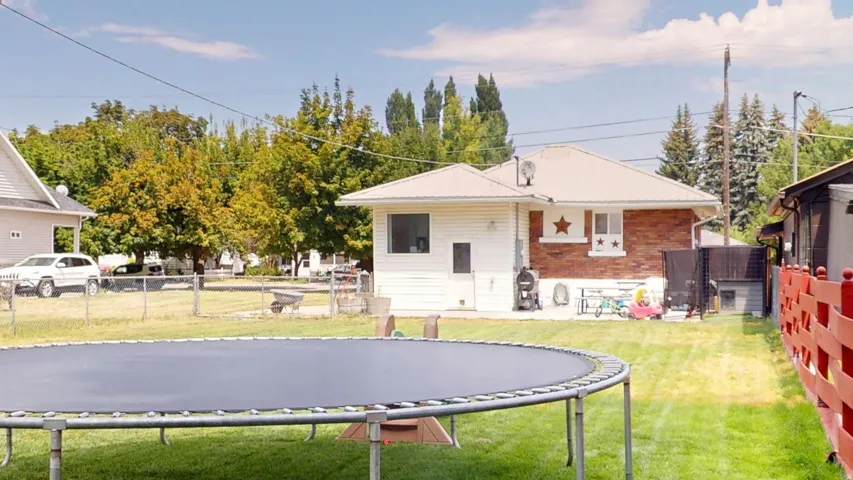 Expansive backyard featuring a manicured lawn, partial chain link fencing, a red wood fence, a white vinyl-sided exterior, and a brick exterior section with white trim
