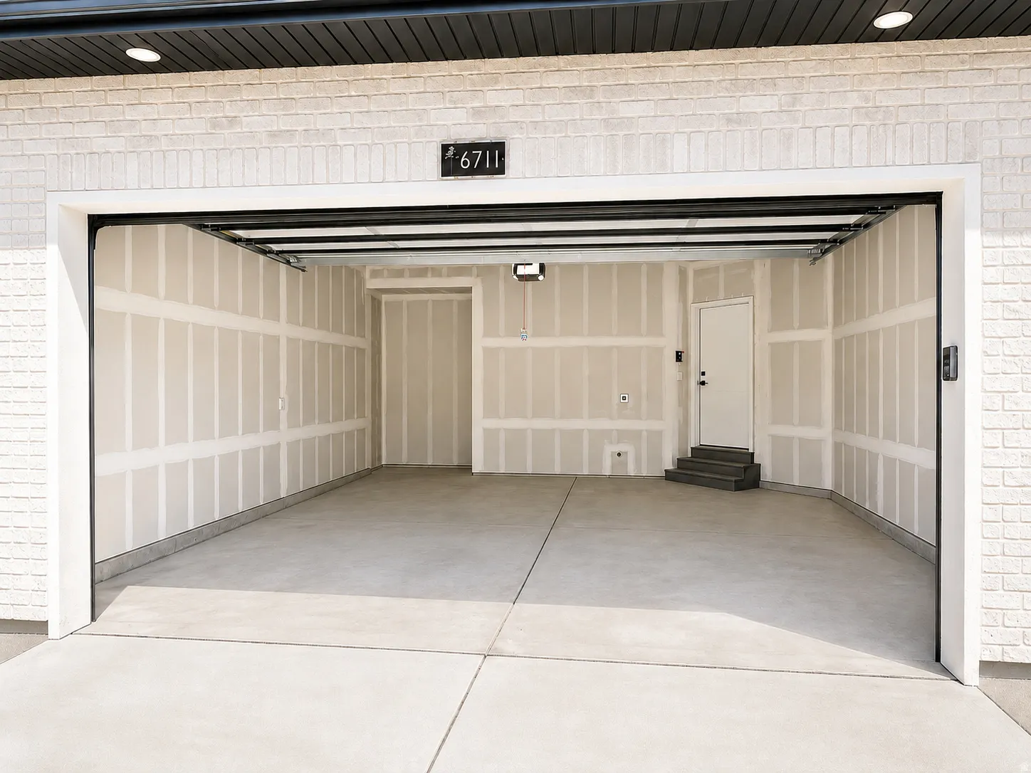 Spacious two-car garage featuring a concrete floor, interior door access, steps, and a white brick exterior