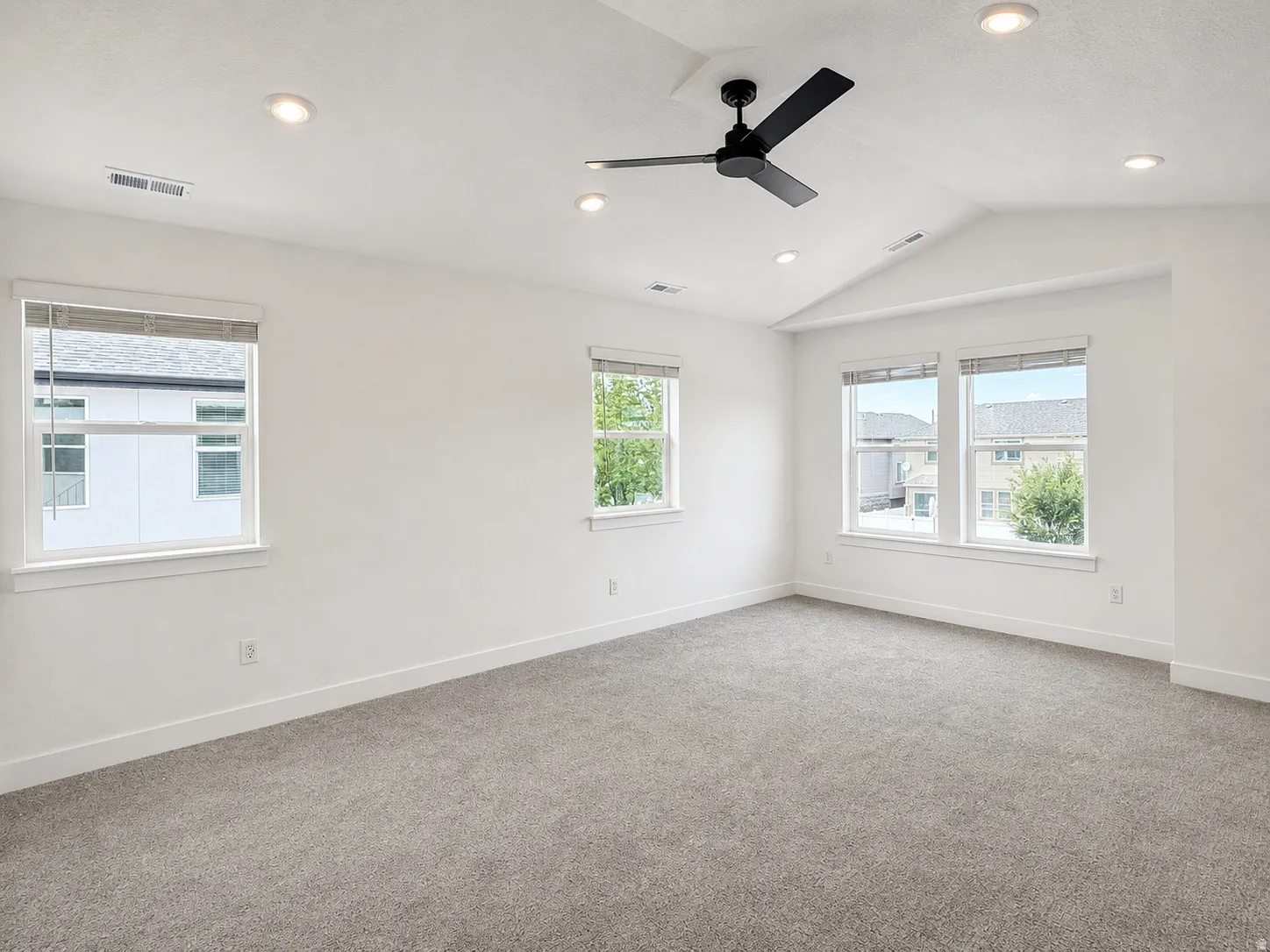 Spacious room featuring vaulted ceilings, a black ceiling fan, recessed lighting, multiple windows with blinds, and gray carpeting