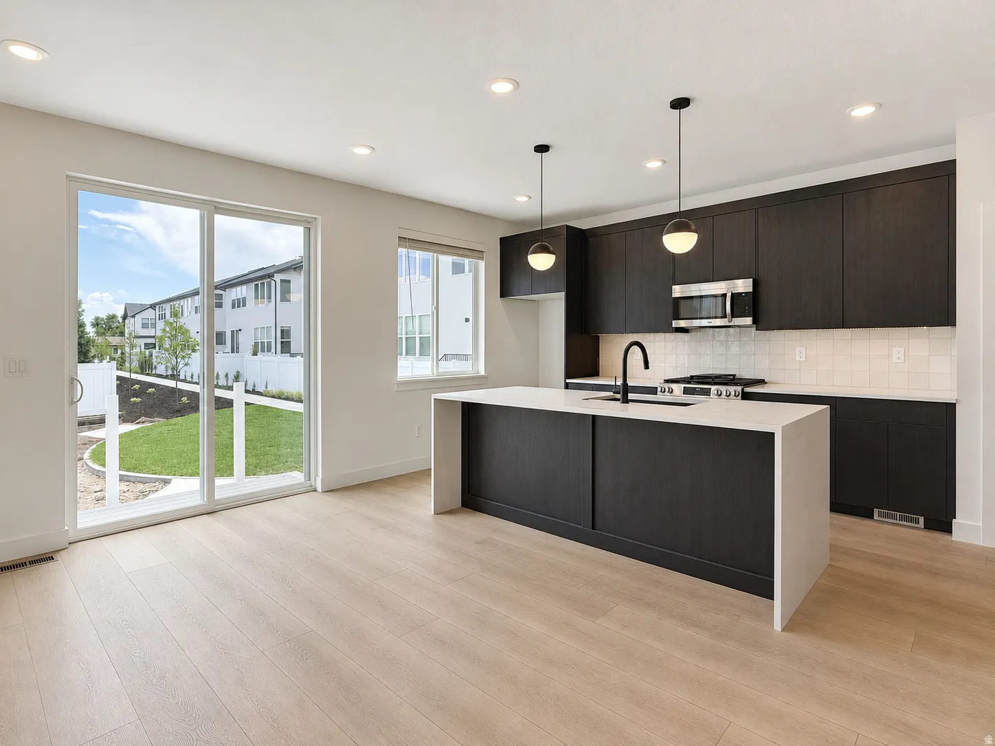 Modern kitchen featuring dark wood-finish cabinetry, a waterfall island with a light-toned countertop, and stainless steel appliances