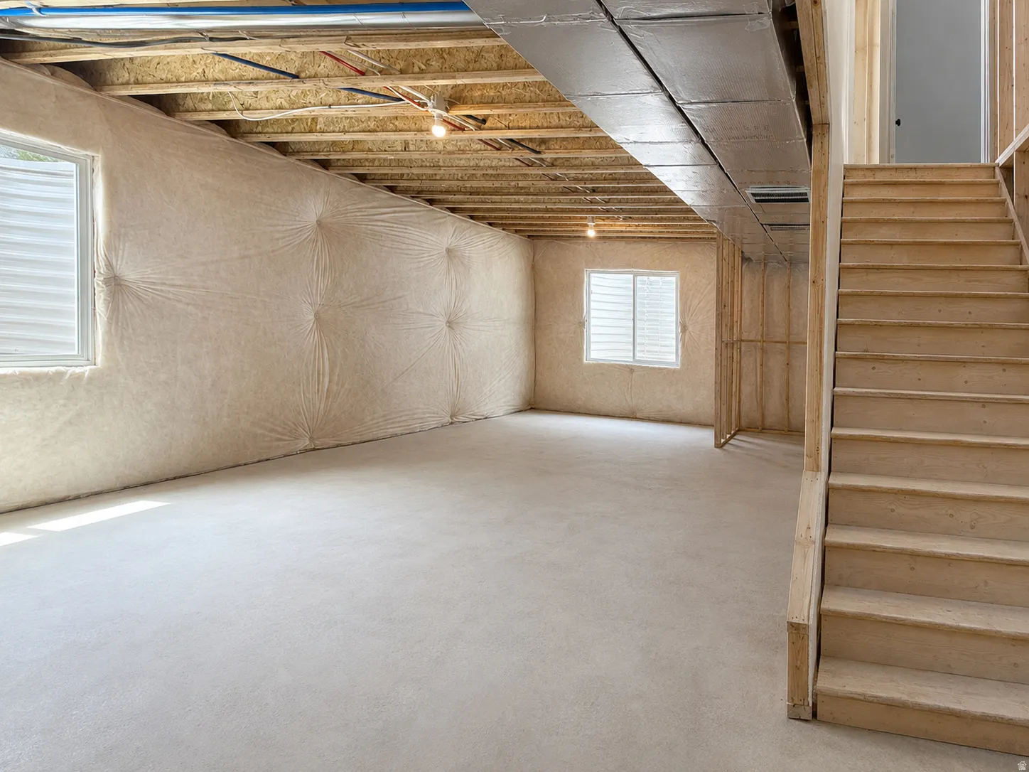 Unfinished lower level featuring an exposed wood joist ceiling, two windows, and a wood staircase