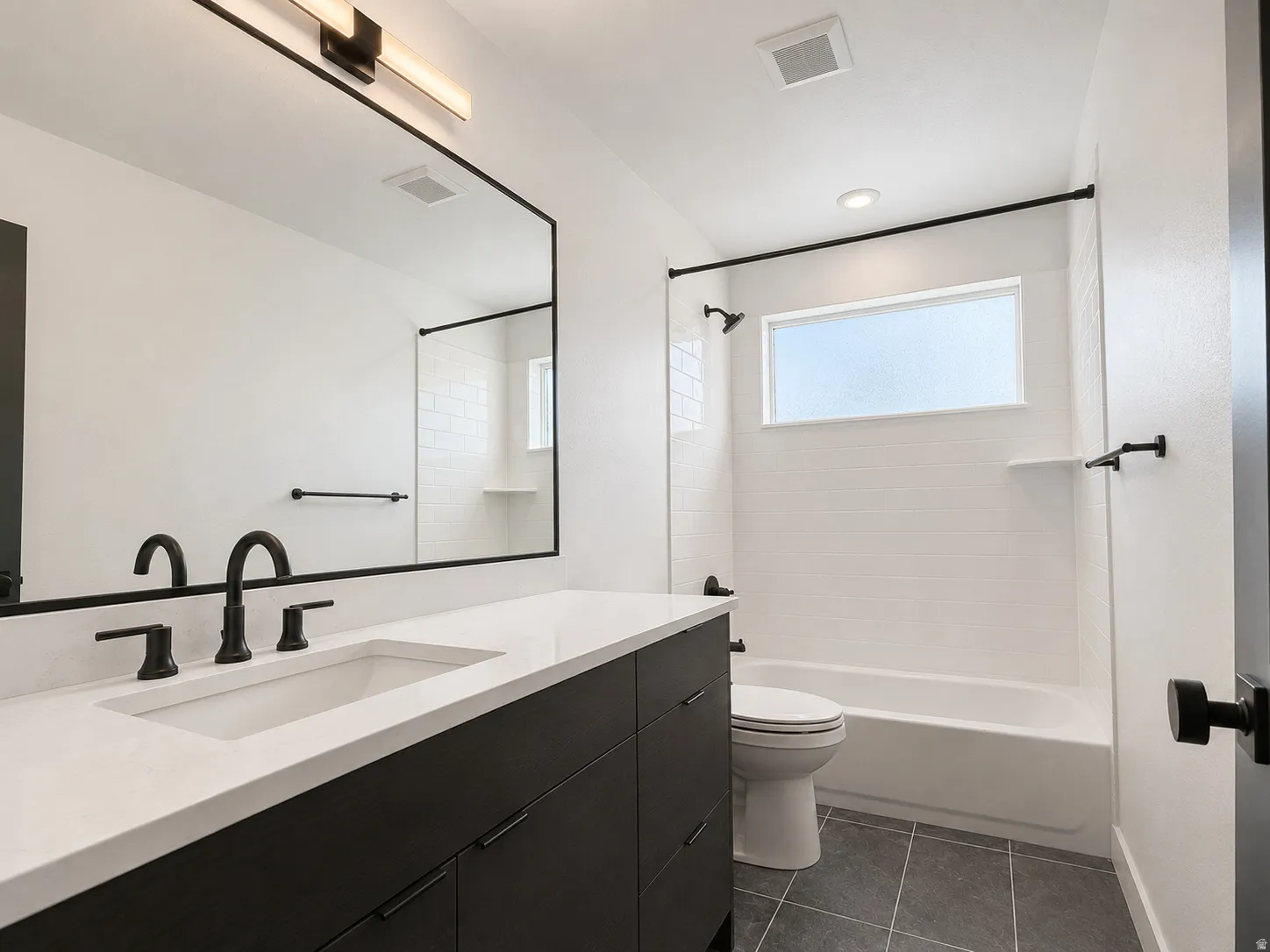 Modern bathroom featuring a single vanity with dark cabinetry, integrated sink, and matte black hardware