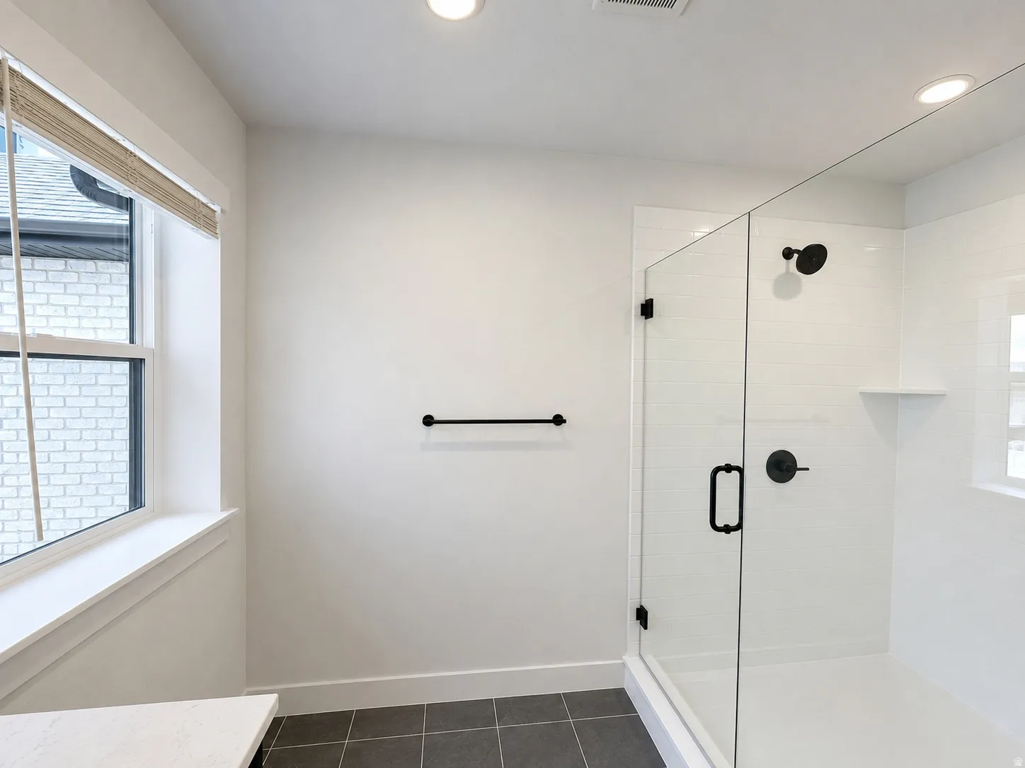 Glass-enclosed shower with matte black fixtures, white subway tile surround, and a built-in shower shelf