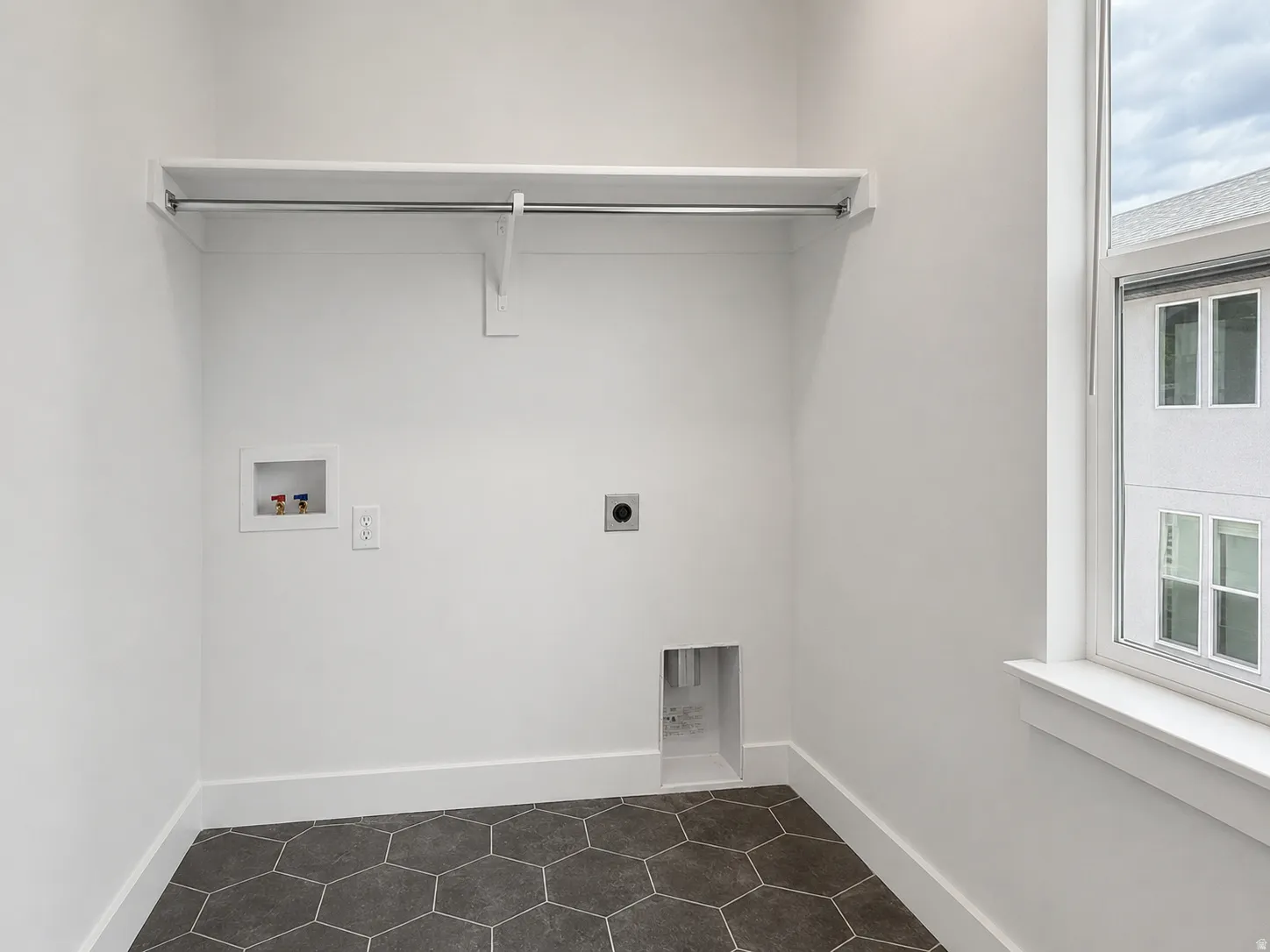 Laundry area featuring hexagonal floor tiling, a white shelf with a hanging rod, dedicated utility hookups, and a window providing natural light