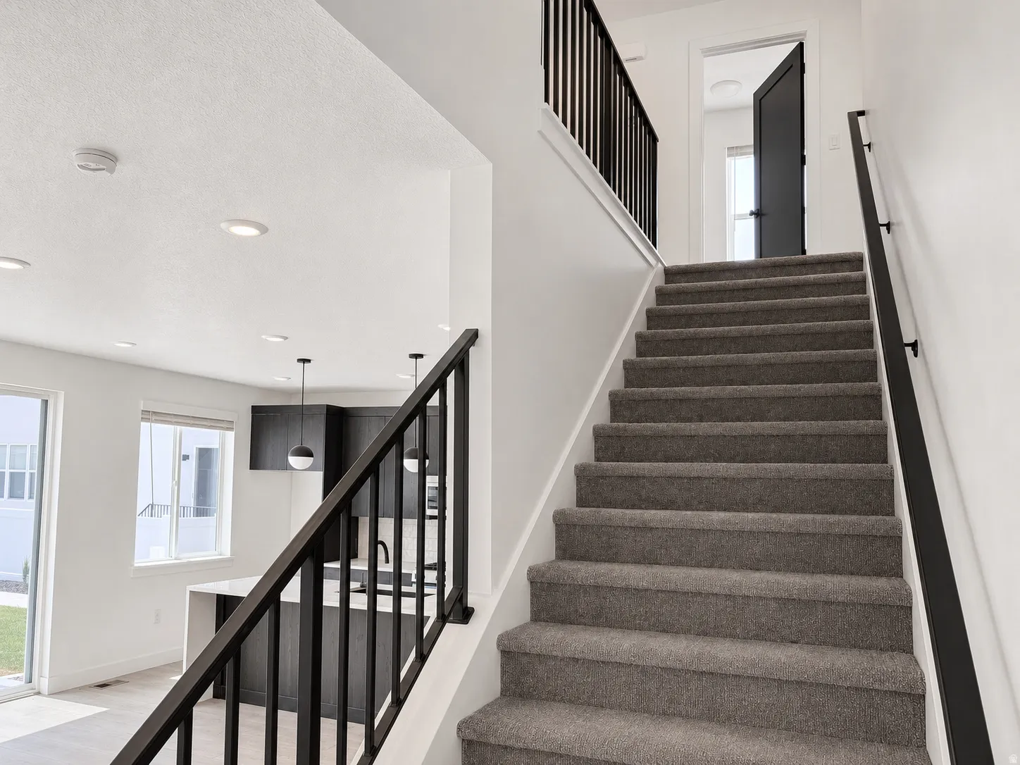 Carpeted staircase featuring a black metal railing and white risers