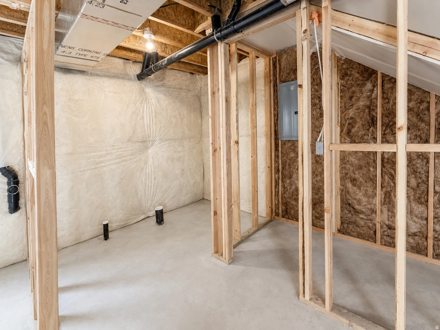 Unfinished basement space featuring visible wood framing, concrete flooring, and insulated walls