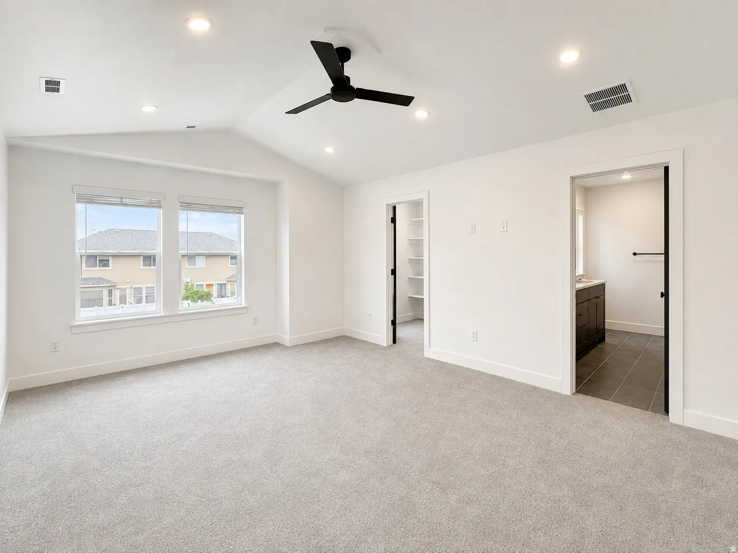 Spacious room with vaulted ceiling featuring a black ceiling fan, recessed lighting, and light grey carpet flooring