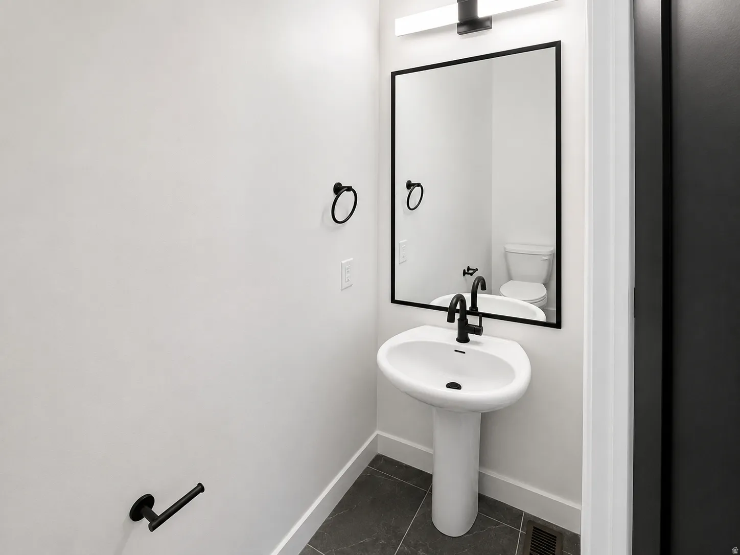 Modern pedestal sink with matte black faucet, framed mirror, and coordinating matte black hardware