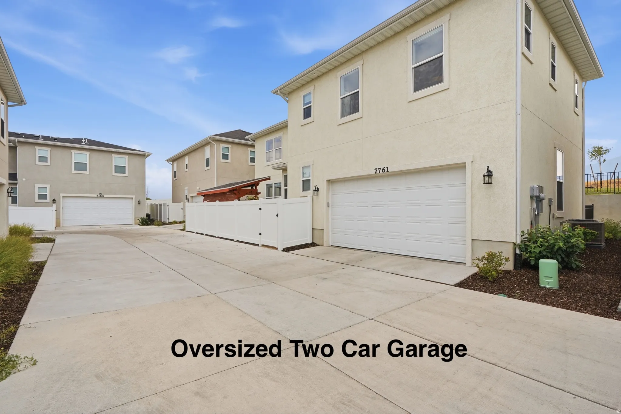 Stucco exterior, two-car garage, concrete driveway, white vinyl fencing, exterior lighting fixtures
