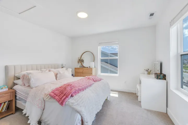 Bright bedroom featuring two windows, light-toned carpeting, and a recessed ceiling light