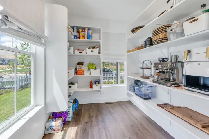 Walk-in pantry featuring extensive built-in shelving, wood-finish flooring, two windows with blinds, and white shiplap wall accents