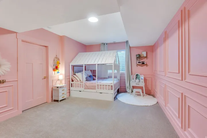 Bedroom featuring light pink walls with wainscoting and trim, grey carpet flooring, a window with drapery, and a three-panel interior door