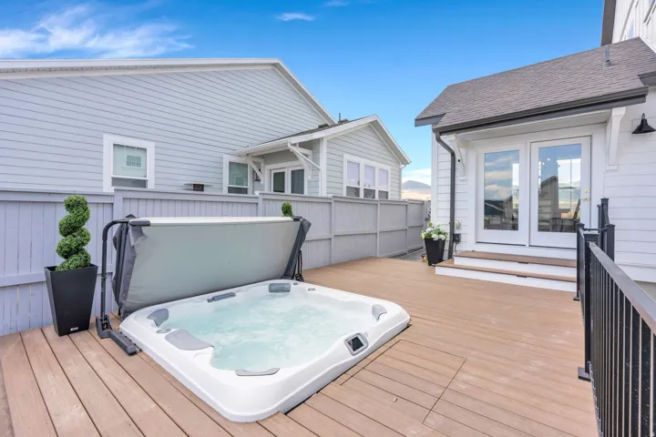 Outdoor deck featuring a built-in spa with cover, multi-panel glass doors, and black metal railings