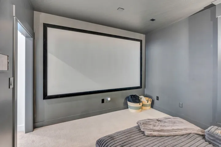 Dedicated media room featuring a large projection screen with a black frame, recessed ceiling lighting, and light-toned carpeting