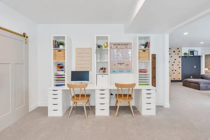 Dedicated study area featuring a built-in desk with multiple drawers, integrated shelving units, and plush carpeting
