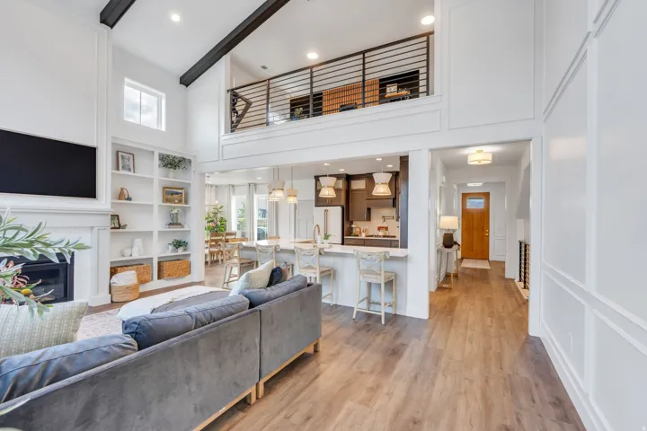 Spacious living area featuring a vaulted ceiling with exposed beams, fireplace with mantle, built-in shelving, and wood-finish flooring